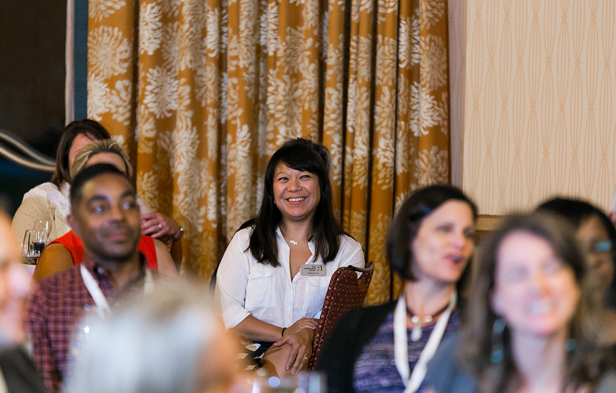 Photo of Marina Lin, Managing Director of Programs, smiling while listening to a speaker.
