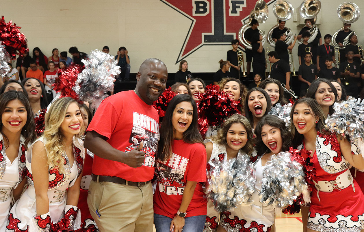 Dr. Andree Osagie posing for a picture with cheerleaders in a school gym.