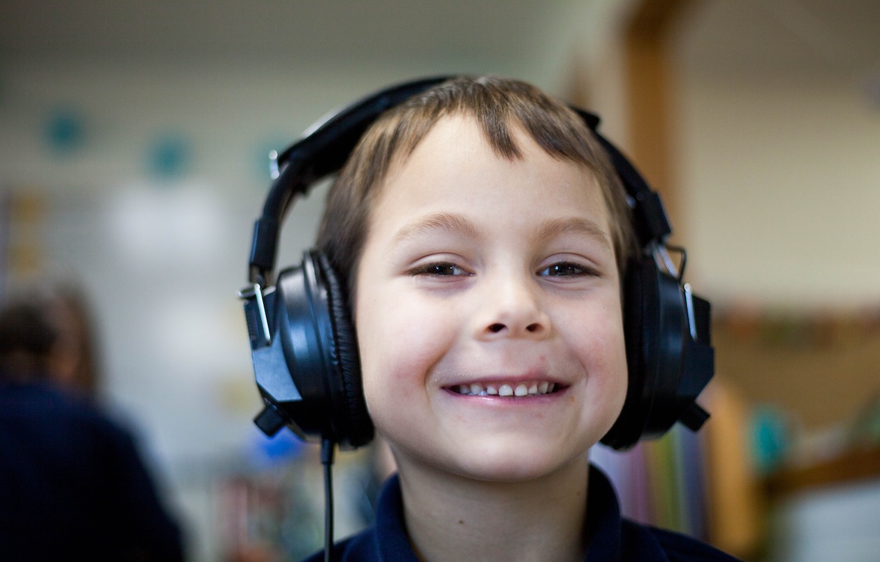 Young boy smiling and wearing headphones.