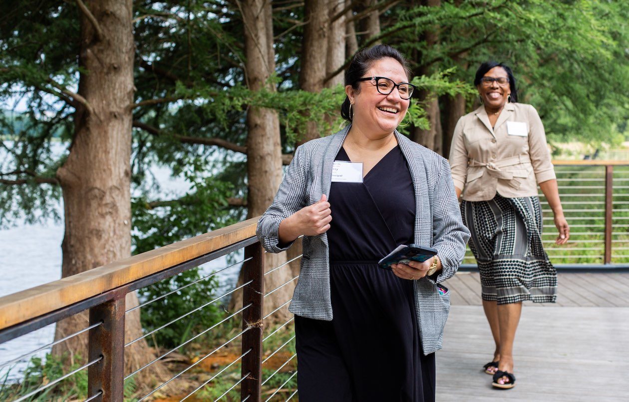 Betty Zavala, Principal at Kaiser Elementary in Klein ISD, and Hazel Berry, Assistant Principal at Kaiser Elementary in Klein ISD, are photographed smiling as they walk along a bridge at the Campus and Lake Austin during a Holdsworth Center Campus Leadership Program session.