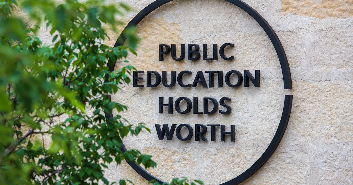 A large metal badge on the exterior administrative building of the Campus at Lake Austin reads public education holds worth.