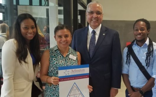 Claudia Morales-Herrera of Carter Junior High School in Arlington ISD, and Dr. Marcelo Cavazos, Superintendent of Arlington ISD, are photographed smiling with colleagues as Claudia holds up an Arlington ISD leadership definition poster.