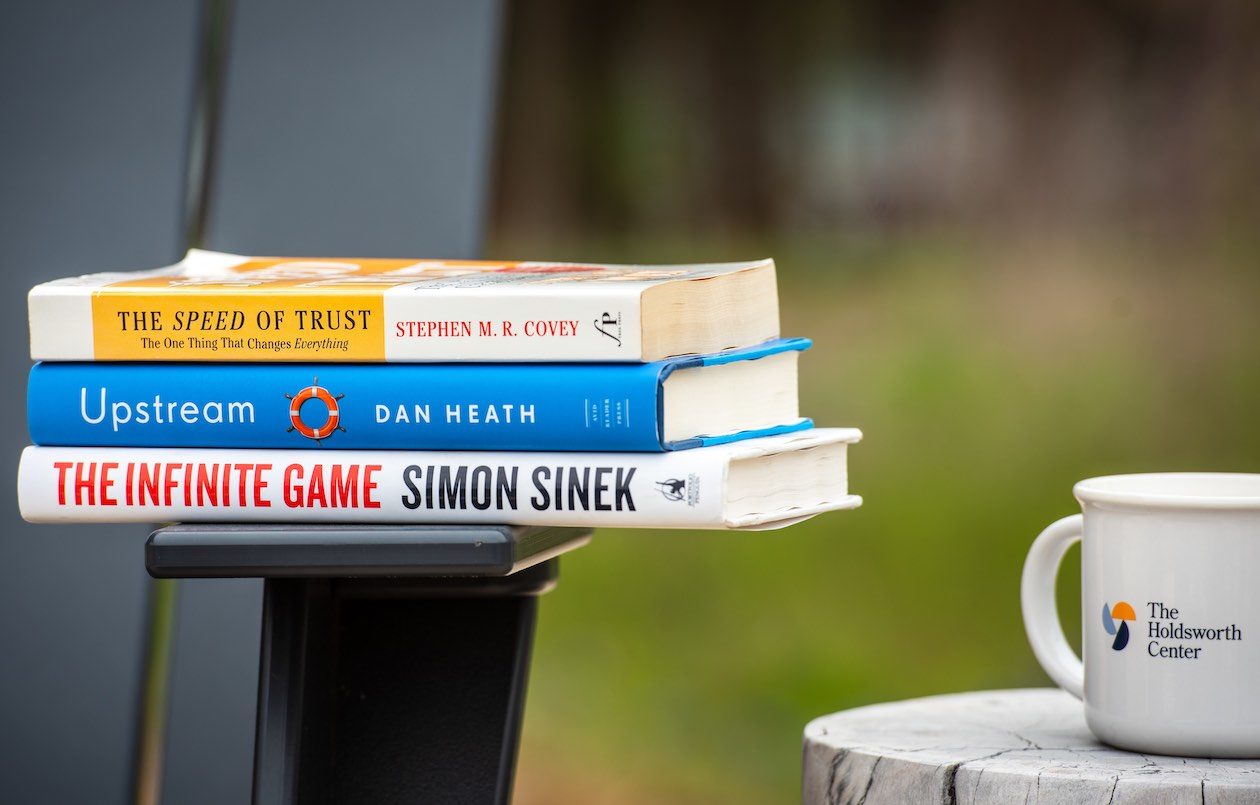 A photos of books stacked on a chair next to a Holdsworth Center coffee mug.